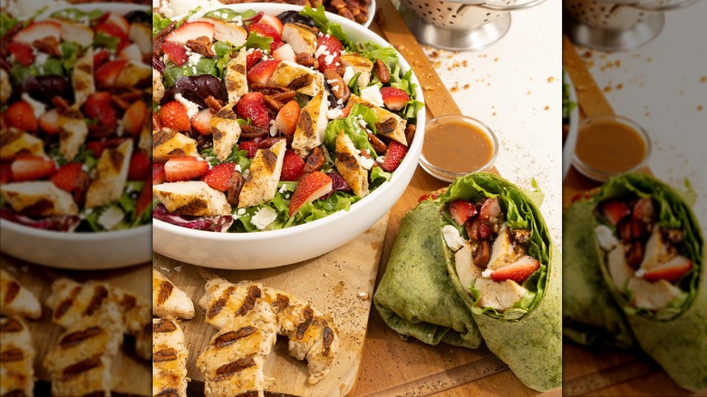 Grilled chicken and strawberry salad at Slim Chickens in a white bowl accompanied by a grilled chicken wrap and grilled chicken tenders