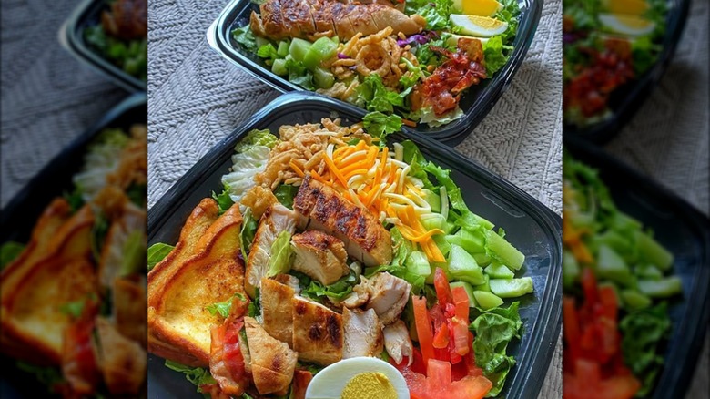Two chicken cobb salads with toast in black to-go containers from Zaxby's