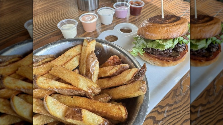French fries with several dipping sauces on the side, beside a burger from Boise Fry Company