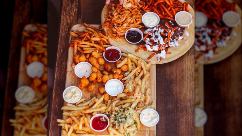 Two platters featuring several types of french fries and tater tots with various dipping sauces from Black Sheep Burgers & Shakes