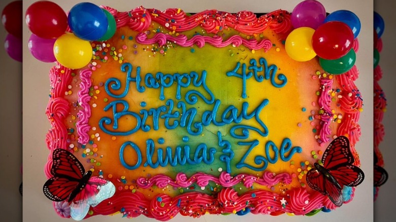 Colorful frosted birthday sheet cake with pink borders, butterflies and balloon toppers