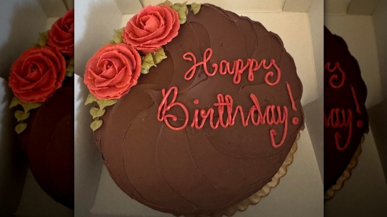 Round cake with chocolate frosting, red roses, and "happy birthday" written in red icing