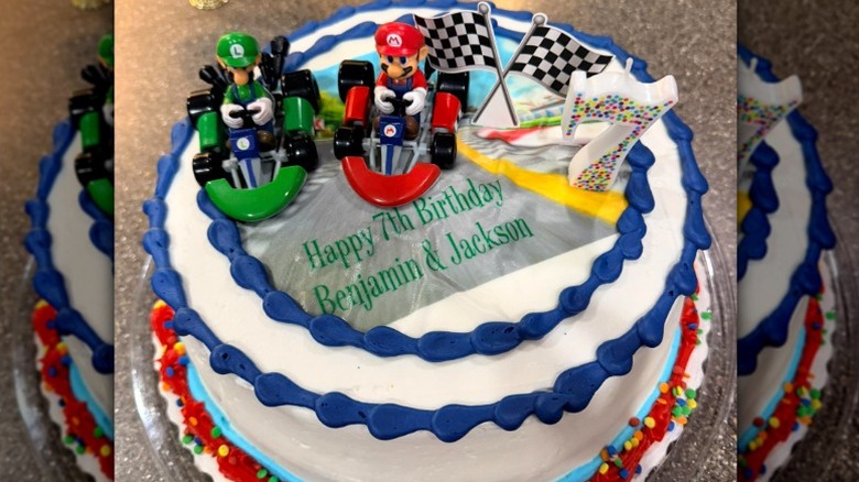 Round white-frosted birthday cake with blue borders and mario and luigi mario kart figurines