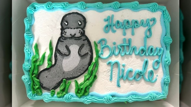 White-frosted happy birthday sheet cake with blue borders and a manatee design