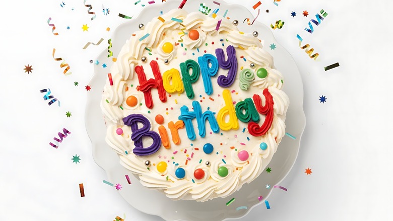 Round birthday cake with white frosting and rainbow writing 