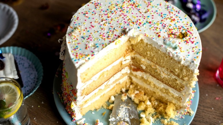 A sliced round yellow cake with white frosting and rainbow sprinkles