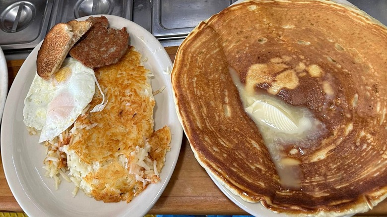 One plate of hash browns, sausage patty, toast, and eggs beside one plate of pancakes at Morg's Diner