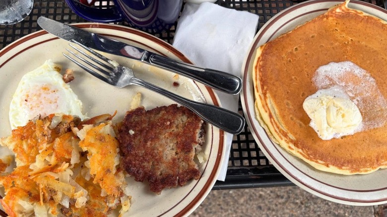 Plate of Pancakes beside a plate of hash browns, fried egg, and breakfast sausage at Our Kitchen