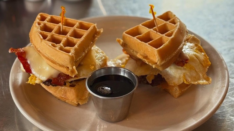Smash patty, bacon, American cheese, and fried egg between a waffle and a side of syrup at Nadeen's Hermitage Haven