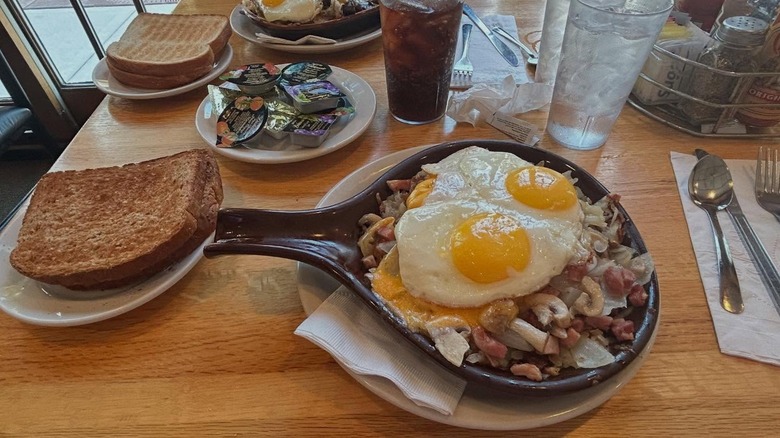 Breakfast skillet with meat and fried eggs, with plates of toast sitting on wooden table at S&G Restaurant