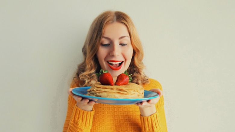 Portrait of a woman holding a plate of pancakes with strawberries on top