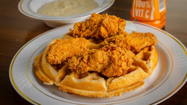 fried chicken wings and a Belgian waffle with bowl of grits in background at  Sugar's Place
