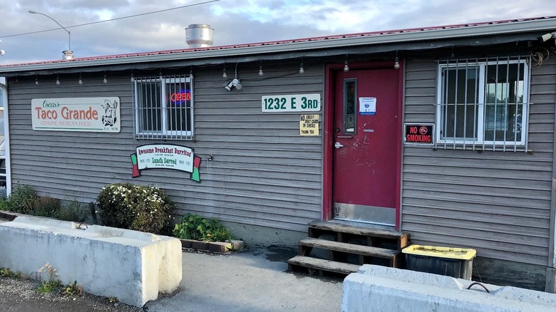 The exterior of a single-story building with gray siding and a red door