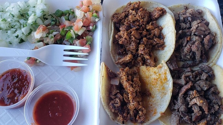 Four tacos in a styrofoam container with pico de gallo and salsa