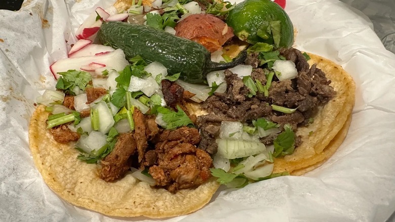 Two tacos on corn tortillas on a piece of white waxed paper