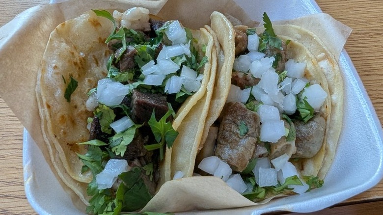 Two tacos in double corn tortillas in a styrofoam container lined with wax paper