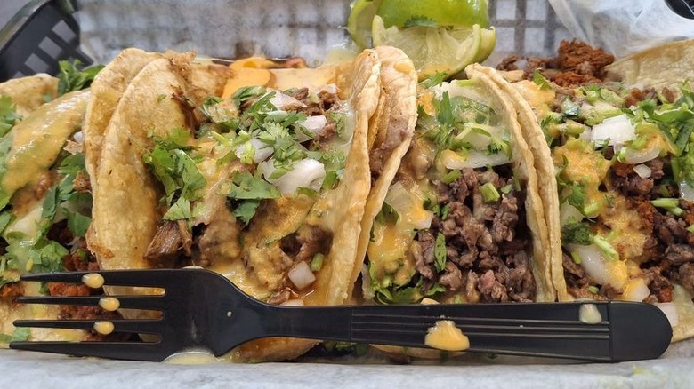 Four tacos on double corn tortillas in a black plastic wax-paper lined oblong basket
