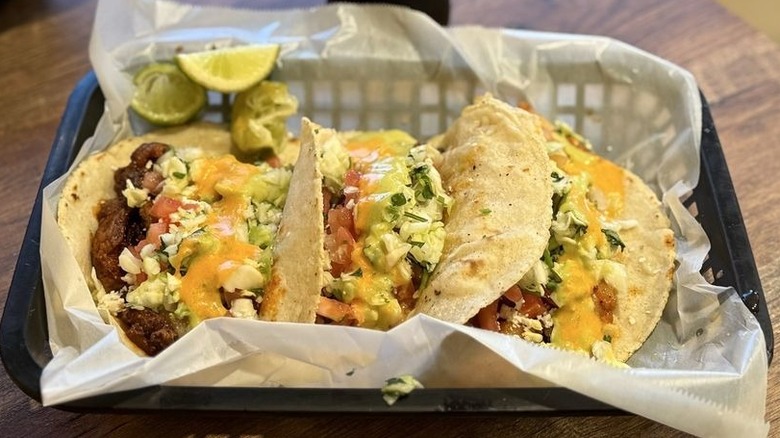 Three tacos on corn tortillas in in a black plastic wax-paper lined rectangular basket
