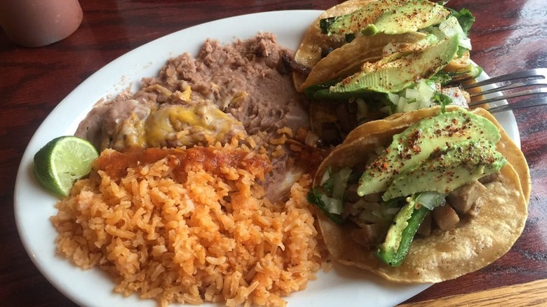 An oval-shaped white plate with refried beans at the top left and Spanish rice and a lime wedge