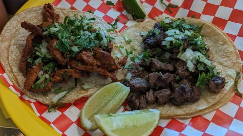 Two tacos in double corn tortillas on a yellow plate lined with red and white checkerboard wax paper