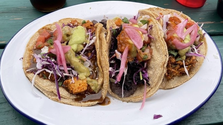 Three tacos on double corn tortillas on a white oval plate set on a blue wooden table