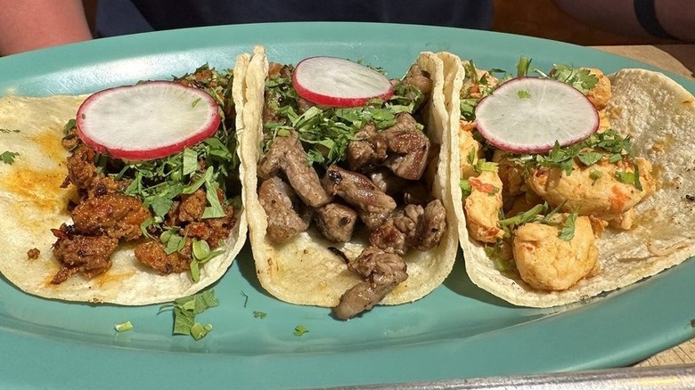 Three tacos on corn tortillas on an oval-shaped aqua plate