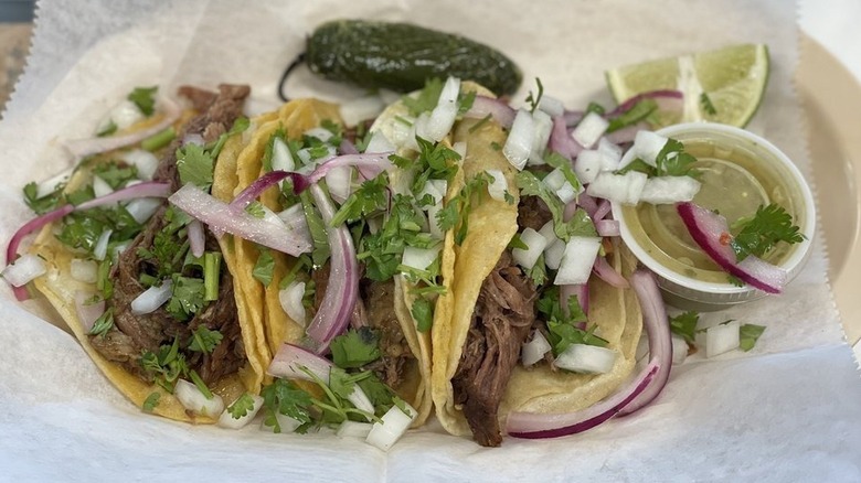 Three shredded beef tacos in double corn tortillas on a white plate topped with chopped white onion