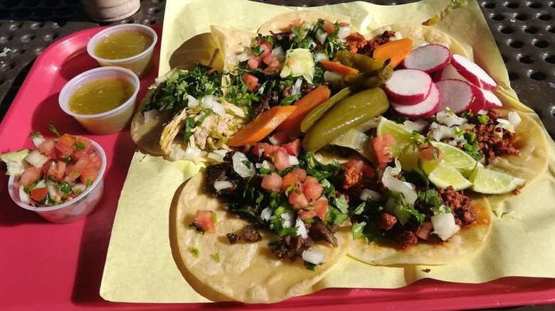 A number of catos on corn tortillas atop a square piece of yellow butcher paper atop a red cafeteria tray