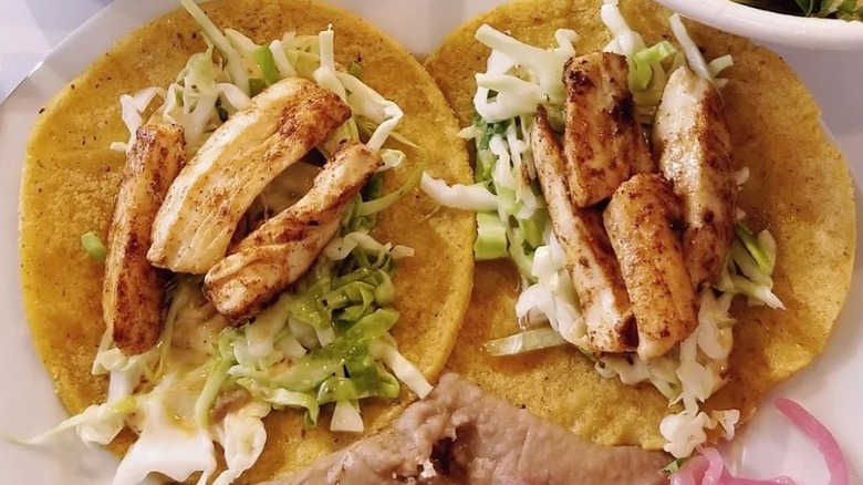 Close-up of two grilled fish tacos on corn tortillas with shredded cabbage