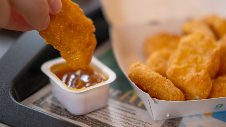 A hand dipping McDonald's chicken nuggets in an unlabeled sauce cup