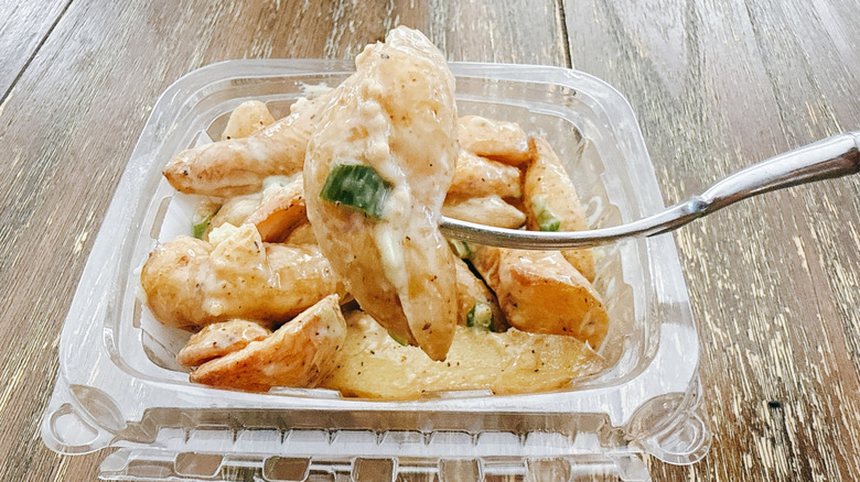 Whole Foods Champagne Dijon Potato Salad on fork with the container in the background on a wooden table