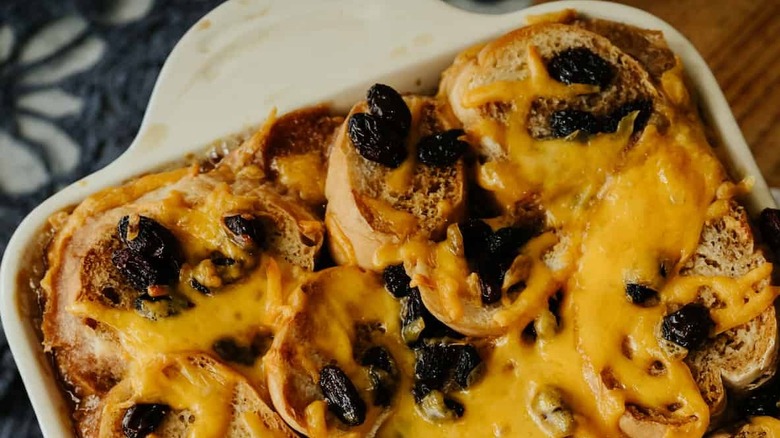 A close-up of a baked bread pudding topped with raisins and a custard sauce