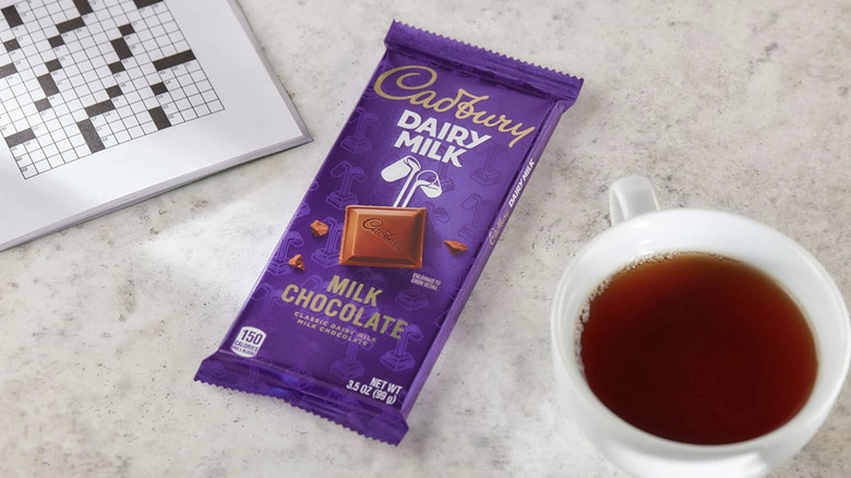 An unopened Cadbury Milk Chocolate Bar sitting next to coffee and crossword puzzle.