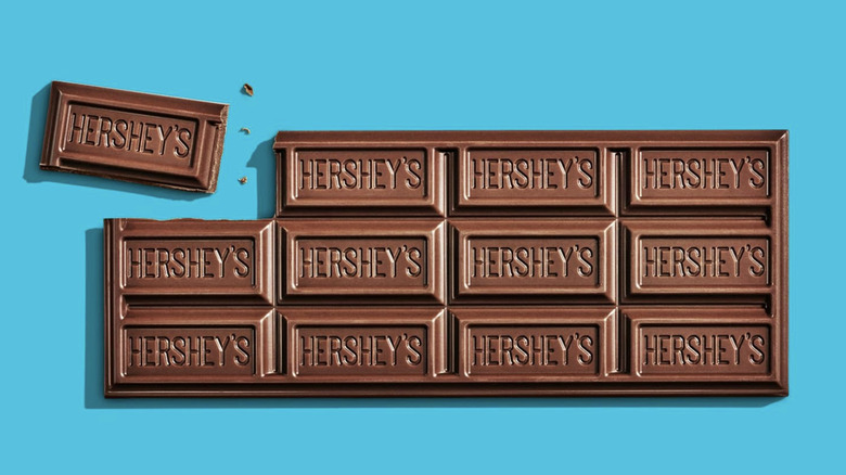 An opened classic Hershey's Milk Chocolate Candy Bar with a smaller block ripped apart and displayed against a baby blue background.