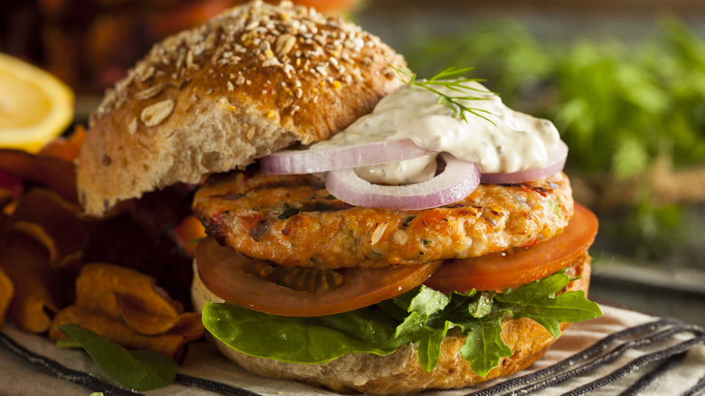 salmon burger on a whole wheat bun with lettuce, tomato, onions, and tartar sauce