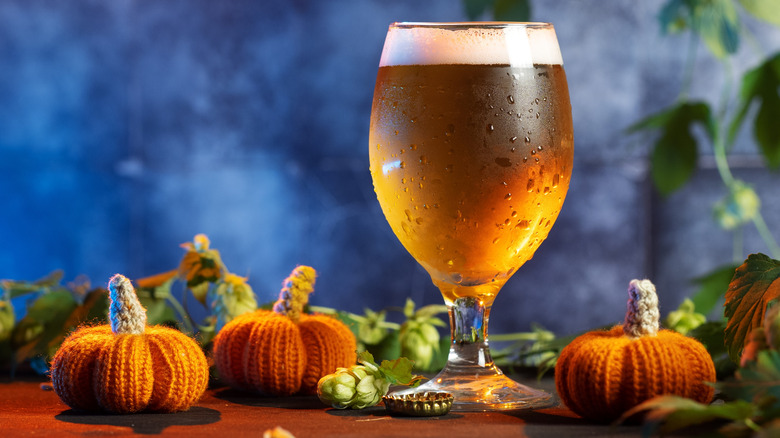 pumpkin beer in a glass surrounded by knitted pumpkin decorations