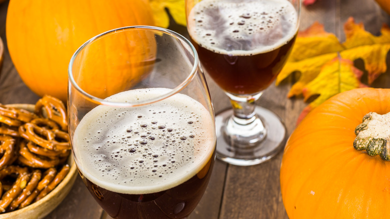 glasses of pumpkin beer with pumpkins, leaves, and a bowl of pretzels