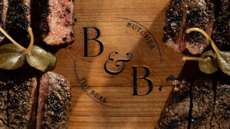 A wooden platter engraved with B & B (Butcher and the Bear) topped with meat