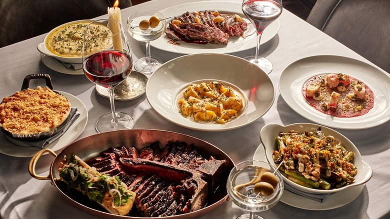 A table set with steak, pasta, sides, glasses of wine and a martinis