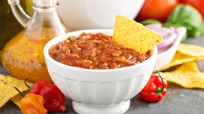 A bowl of red salsa with a corn chip dipped in it.