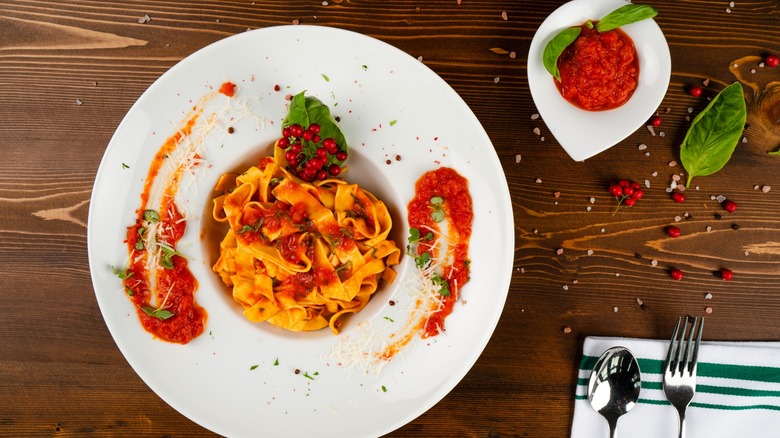 Fettuccini pasta with tomato sauce in white bowl with tomato sauce on the side