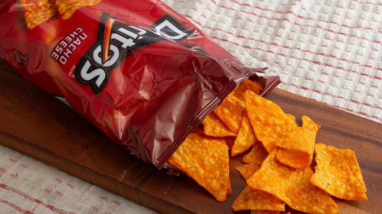 Open bag of Doritos spilling out onto a wooden cutting board
