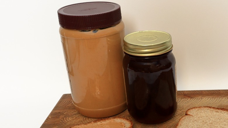 jars of peanut butter and jelly on a wooden board with sliced bread