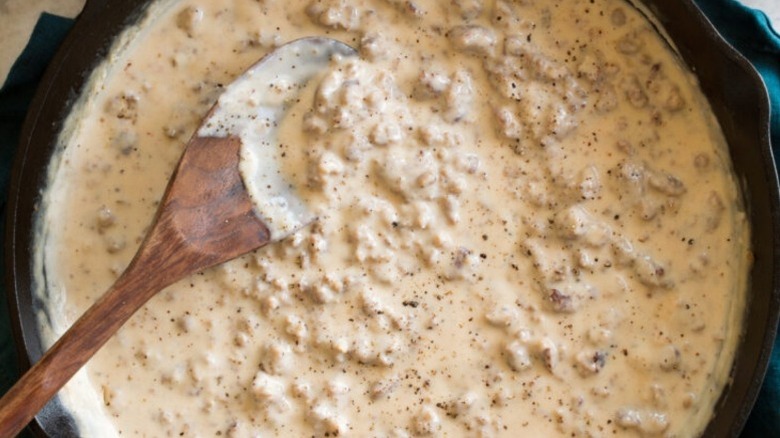sausage gravy in a black pot with a wooden spoon