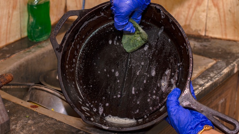 Person washing cast iron pan with soap and sponge