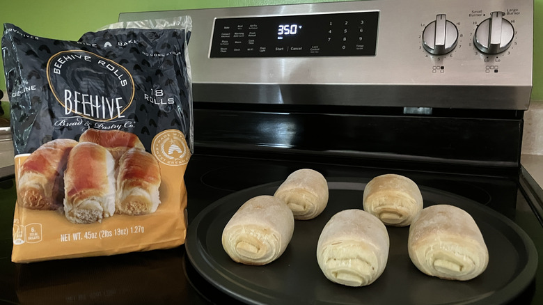 A bag of frozen Beehive Rolls on a stove top next to a pan of baked rolls, with the ends aimed forward to show the rolled dough