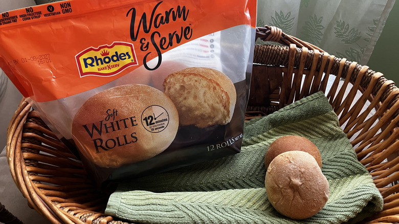 a bag of Rhodes Warm & Serve soft white bread rolls in a basket with two baked rolls