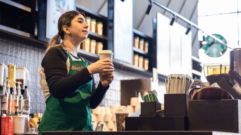 A Starbucks worker with a coffee in her hand wearing a green apron