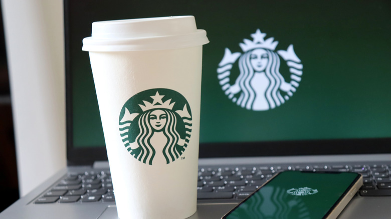 A Starbucks coffee cup beside a smartphone and laptop with the Starbucks logo on them