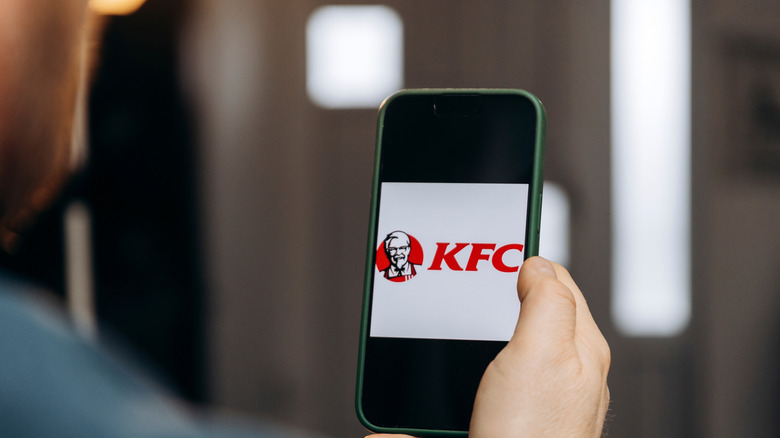 A person holds a phone with the KFC logo on the screen